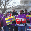 ATC workers in purple shirts stand before the U.S. Capitol carrying signs that read 'Stop the Shutdown', 'Real People Real Consequences', and 'Federal Workers are American Workers', during the US federal government shutdown 2019.