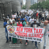 Group of app-based drivers and supporters march in Manhattan holding a banner reading “NEW YORK TAXI WORKERS ALLIANCE” and placards demanding respect, fair pay, and protections for drivers, which would include just cause / deactivation protections. Skyscrapers and city streets frame the organized rally.