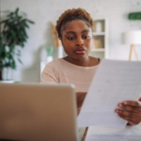 A young Black woman sitting at a desk, working attentively on a laptop, and looking at Unemployment Insurance claim information.